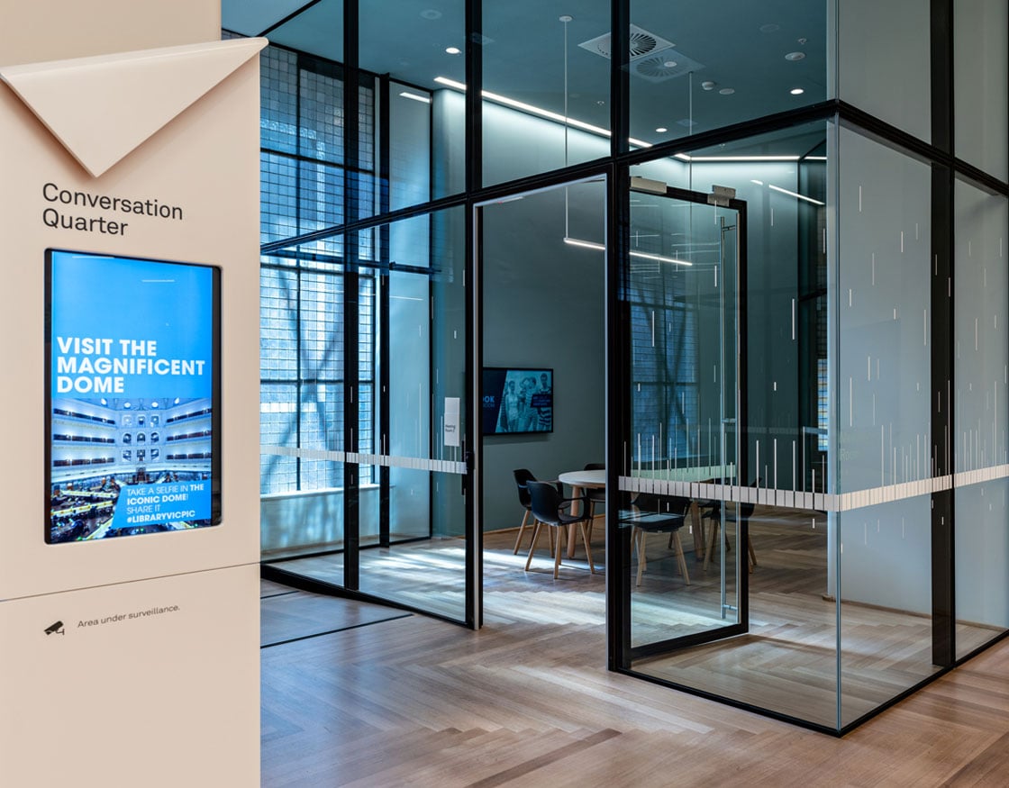 Glass-walled meeting room with a large screen showing digital information.