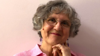 Woman with short grey hair and glasses smiling at camera