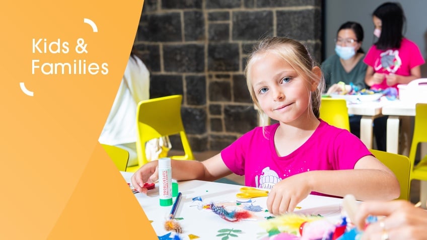 Young girl in hot pink t-shirt smiling at camera, mid-craft activity