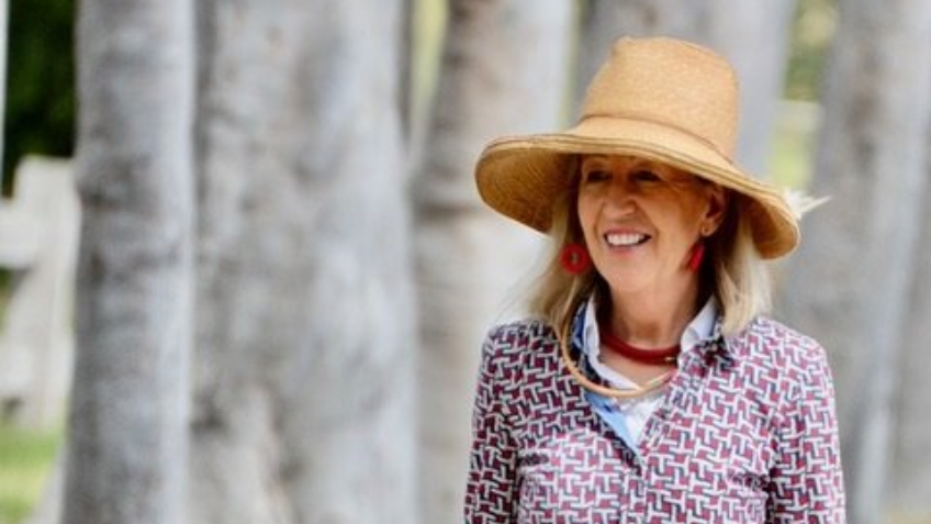 Woman wearing big hat and patterned shirt smiling into the distance