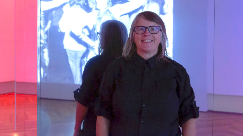 Woman in black button up shirt smiling in front of a large mirror