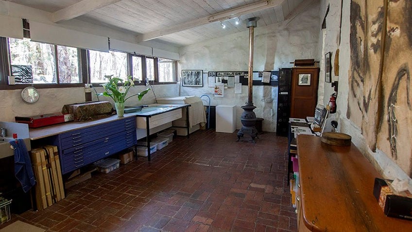 interior shot of printing studio with tiled floor, wooden roof, potbelly stove, sinks, drawers and equipment