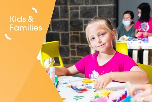 Young girl in hot pink t-shirt smiling at camera, mid-craft activity