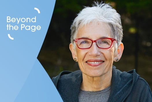 Old woman with short cropped hair and bright red glasses smiling at camera