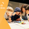 Four primary-school aged kids huddled around a table playing with LEGO pieces.